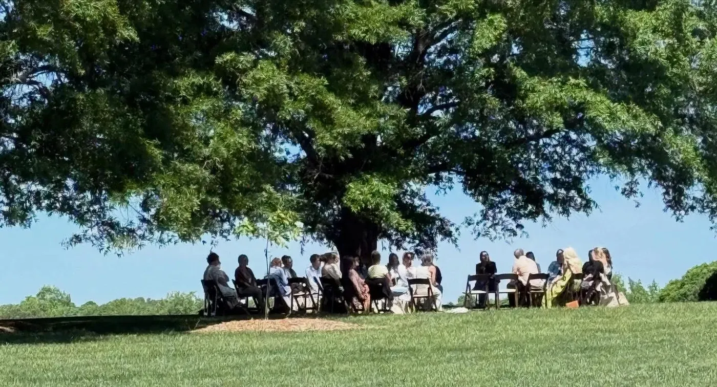 Salon professionals seated in a circle beneath a large shade tree at the Spirit of Hygge gathering in Raleigh