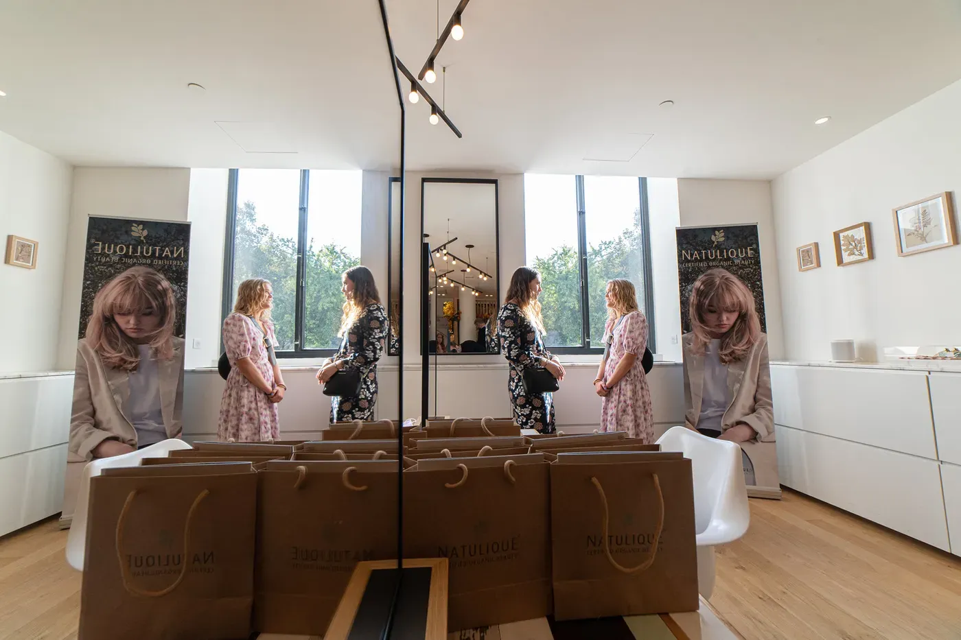 Guests in a NATULIQUE event room with gift bags and NATULIQUE banners, reflected in a mirror